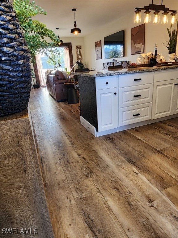 kitchen with white cabinets, open floor plan, dark stone countertops, hanging light fixtures, and light wood-type flooring