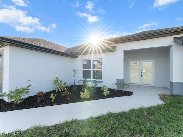 view of side of home with french doors, an attached garage, and stucco siding