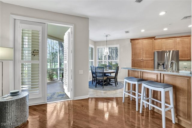 kitchen featuring wood finished floors, visible vents, a kitchen breakfast bar, stainless steel fridge with ice dispenser, and pendant lighting