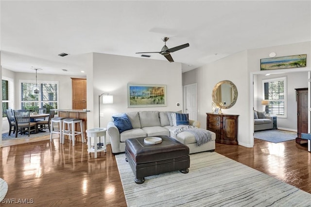 living room featuring a ceiling fan, visible vents, baseboards, and wood finished floors