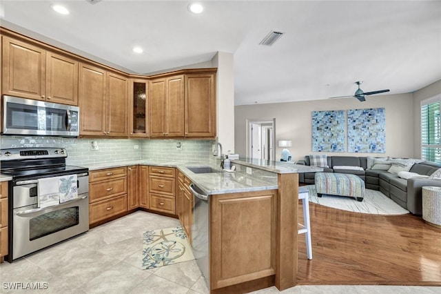 kitchen featuring visible vents, a breakfast bar area, a peninsula, stainless steel appliances, and a sink