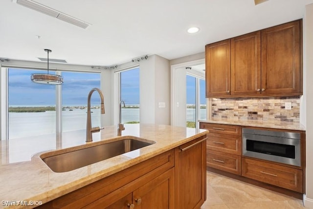 kitchen with light stone countertops, built in microwave, a sink, brown cabinets, and tasteful backsplash