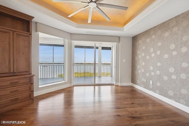 unfurnished room featuring a ceiling fan, baseboards, dark wood finished floors, a raised ceiling, and wallpapered walls