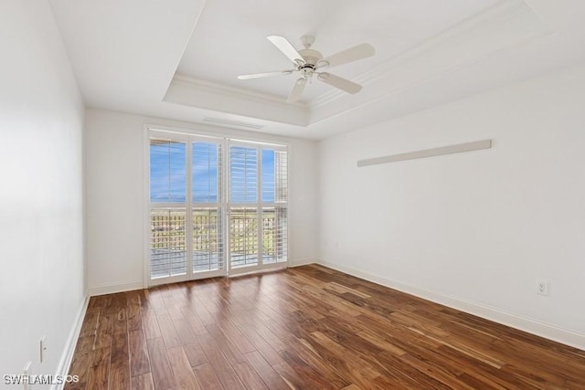 spare room featuring baseboards, a raised ceiling, ceiling fan, ornamental molding, and wood finished floors