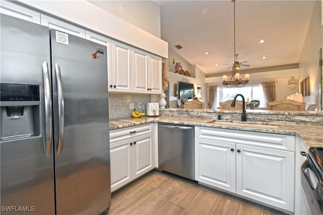 kitchen with decorative backsplash, white cabinets, light wood-style flooring, appliances with stainless steel finishes, and a sink