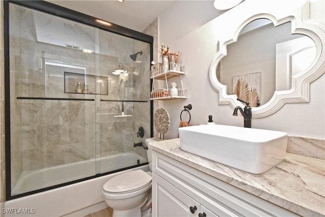 bathroom with bath / shower combo with glass door, vanity, and toilet