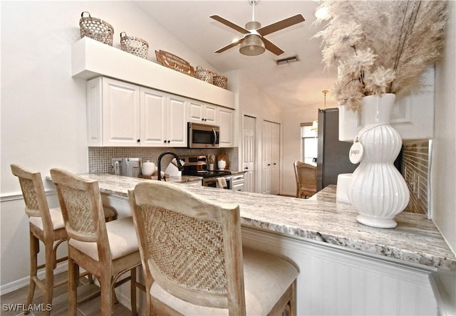 kitchen with visible vents, decorative backsplash, appliances with stainless steel finishes, vaulted ceiling, and a peninsula