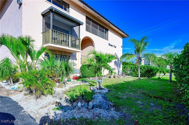 back of house with a balcony, a tile roof, a lawn, and stucco siding