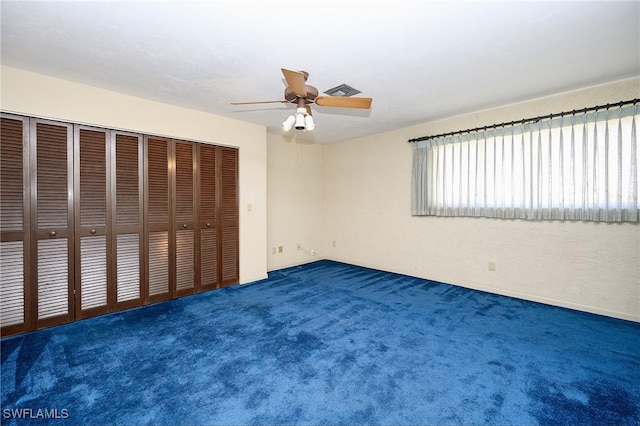 unfurnished bedroom featuring ceiling fan, dark colored carpet, a closet, and visible vents