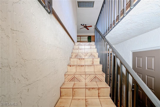 staircase featuring tile patterned flooring, a textured wall, and ceiling fan