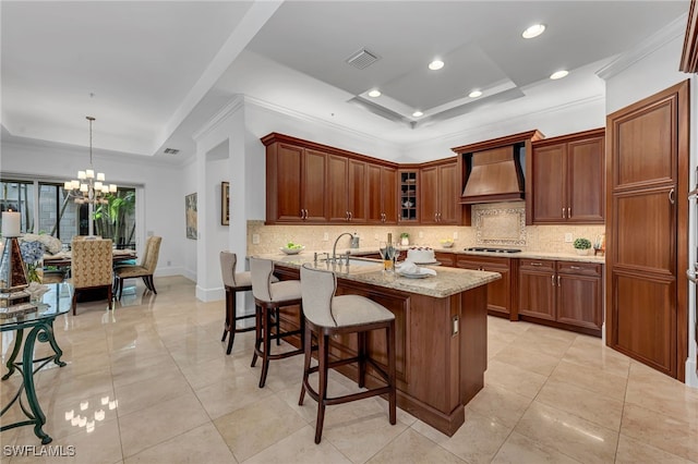 kitchen featuring light stone counters, pendant lighting, a raised ceiling, glass insert cabinets, and premium range hood