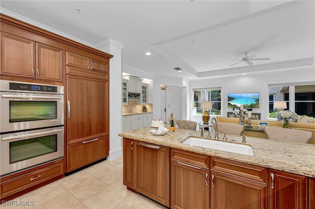 kitchen featuring double oven, light stone counters, a sink, open floor plan, and brown cabinetry