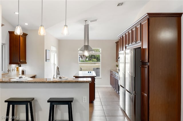 kitchen featuring light tile patterned floors, a peninsula, freestanding refrigerator, a kitchen breakfast bar, and island range hood