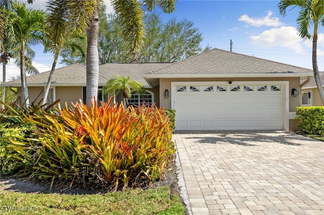 ranch-style home with stucco siding, decorative driveway, a garage, and roof with shingles