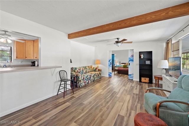 living room featuring light wood finished floors, ceiling fan, baseboards, and beam ceiling