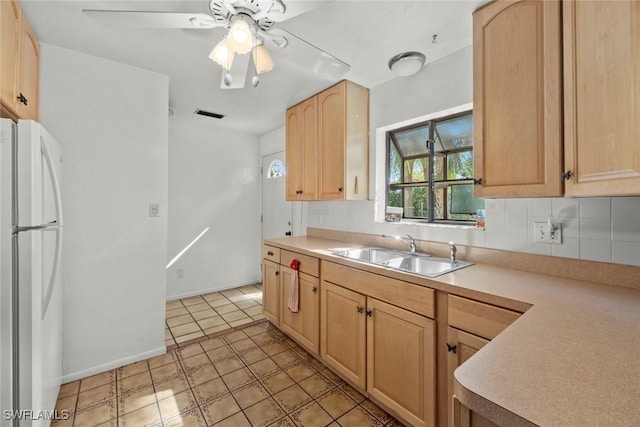 kitchen with light brown cabinets, light countertops, a sink, and freestanding refrigerator