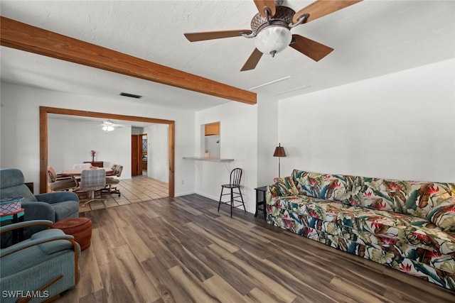 living area with ceiling fan, beamed ceiling, a textured ceiling, and wood finished floors