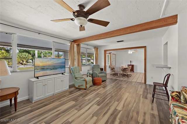 living area featuring light wood-style floors, beam ceiling, visible vents, and a textured ceiling