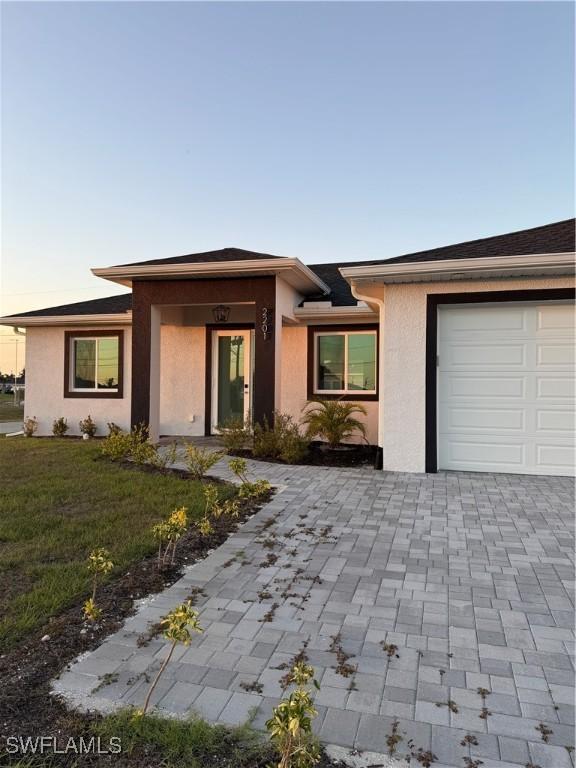 view of front of home featuring a garage, a front yard, decorative driveway, and stucco siding