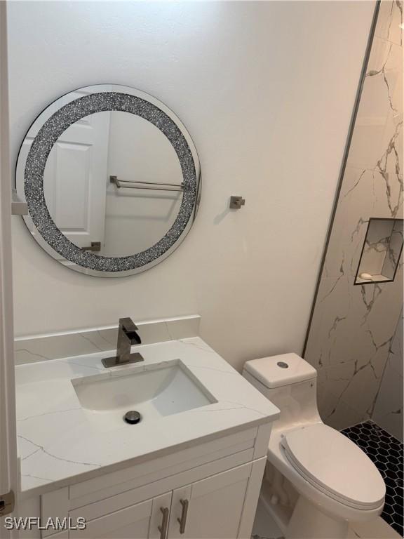 full bathroom with toilet, a marble finish shower, and vanity