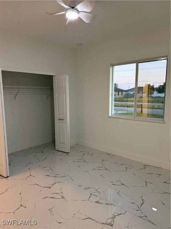 unfurnished bedroom featuring ceiling fan, marble finish floor, a closet, and baseboards