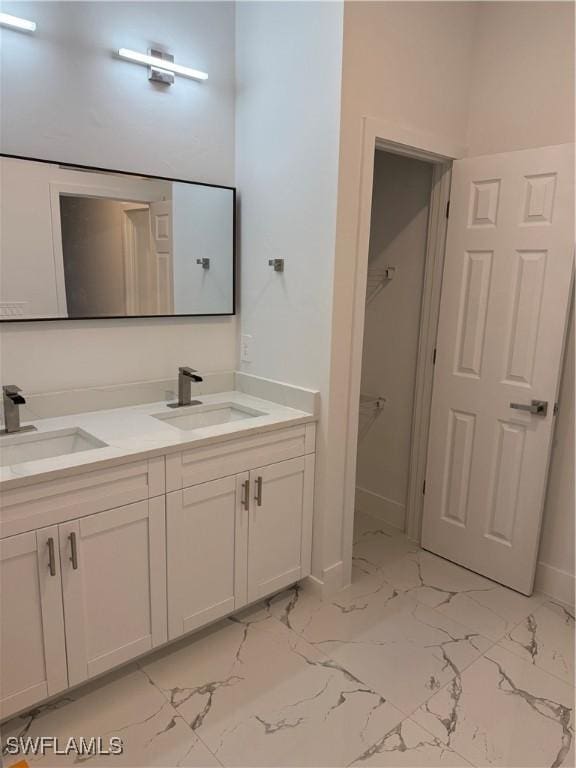 full bathroom featuring double vanity, marble finish floor, baseboards, and a sink