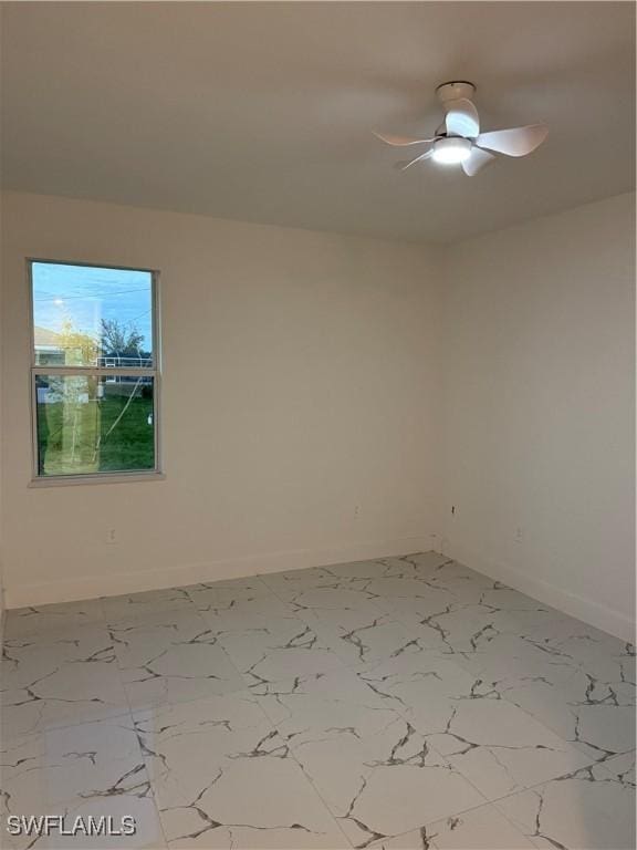 unfurnished room with a ceiling fan, marble finish floor, and baseboards