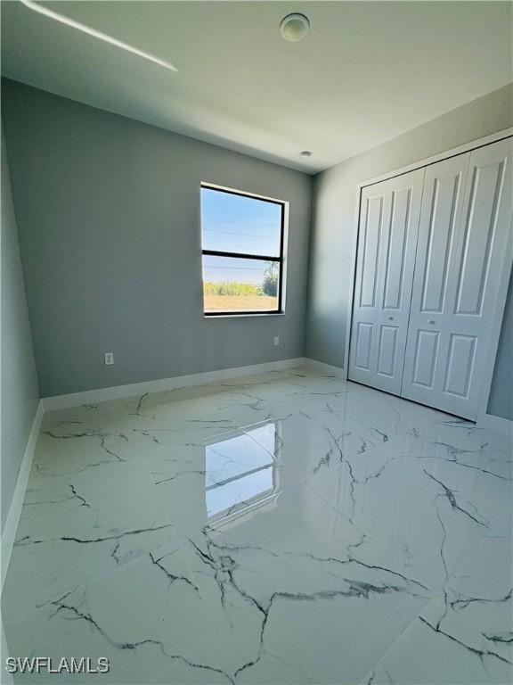 unfurnished bedroom with marble finish floor, baseboards, and a closet