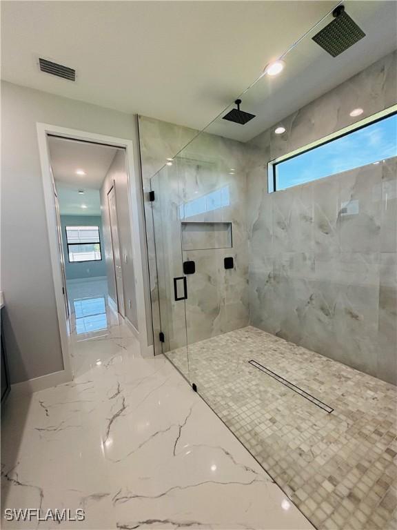 bathroom with marble finish floor, a marble finish shower, visible vents, and baseboards