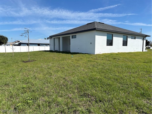 view of home's exterior with a yard, roof with shingles, fence, and stucco siding