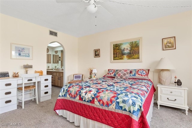 bedroom featuring arched walkways, visible vents, light carpet, connected bathroom, and ceiling fan