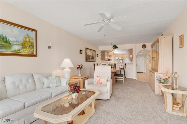 living room featuring arched walkways, light carpet, ceiling fan, and a textured ceiling