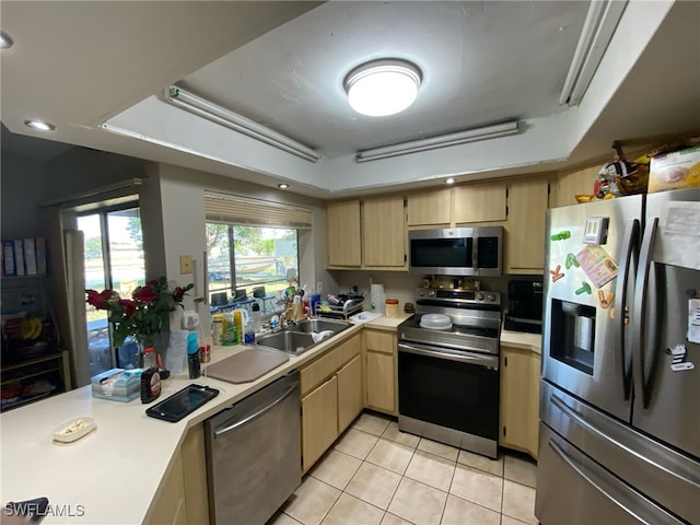 kitchen with stainless steel appliances, a sink, light countertops, light brown cabinetry, and a raised ceiling