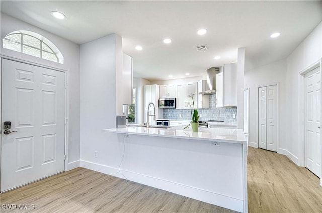 kitchen featuring visible vents, white cabinets, stainless steel microwave, light wood-type flooring, and wall chimney range hood