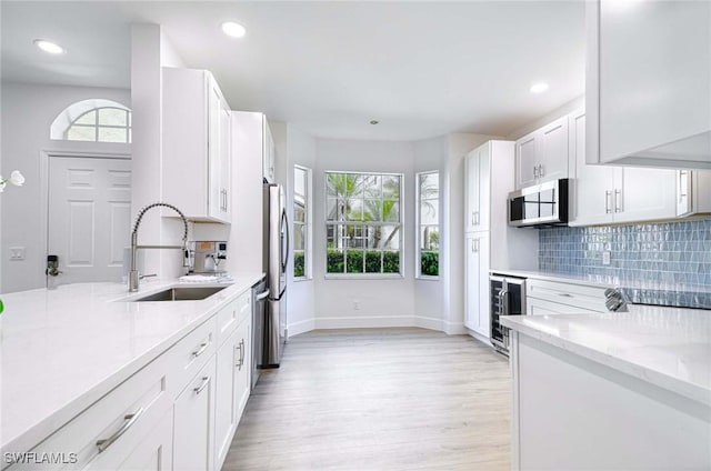 kitchen with light stone countertops, beverage cooler, stainless steel appliances, a sink, and decorative backsplash