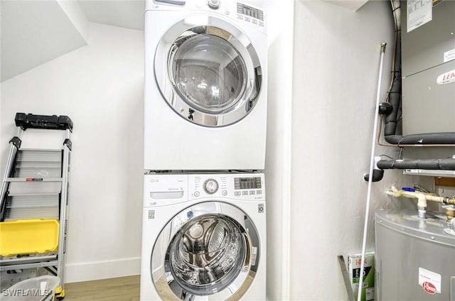 washroom with stacked washer / dryer, laundry area, water heater, and wood finished floors