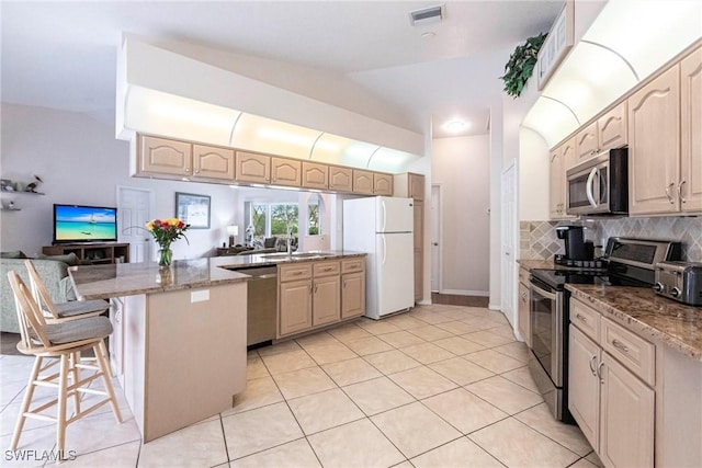 kitchen with visible vents, a peninsula, stainless steel appliances, a kitchen bar, and backsplash