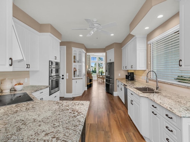 kitchen featuring appliances with stainless steel finishes, light stone counters, dark wood-type flooring, white cabinetry, and a sink