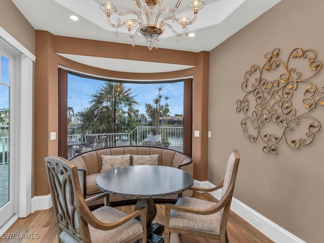 dining area with a water view, baseboards, a chandelier, and wood finished floors