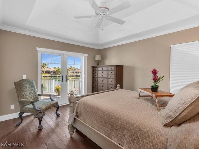 bedroom with a water view, access to outside, a tray ceiling, and wood finished floors