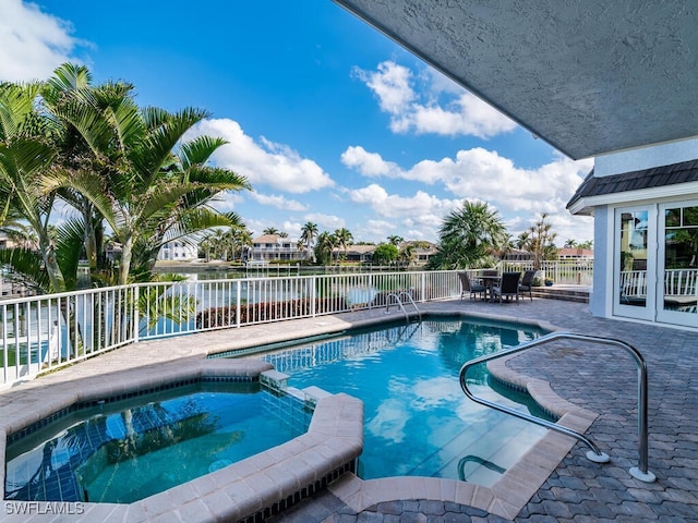 view of swimming pool with a patio area, a pool with connected hot tub, a water view, and fence