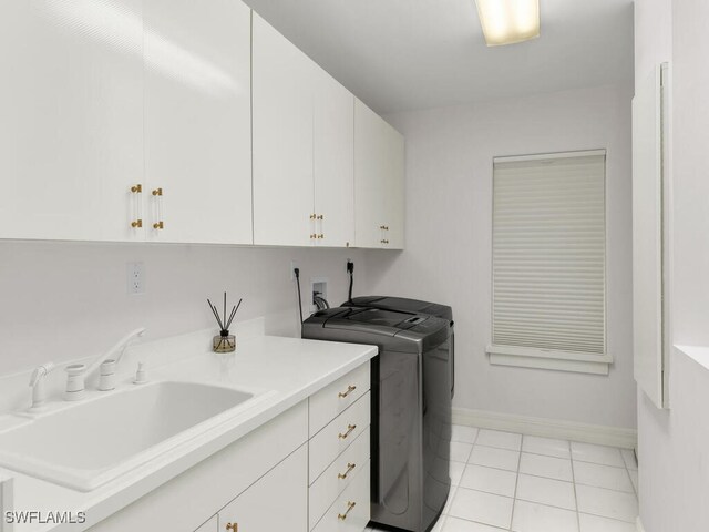 clothes washing area with light tile patterned floors, separate washer and dryer, a sink, baseboards, and cabinet space