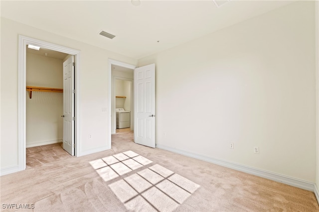 unfurnished bedroom featuring a walk in closet, washer / clothes dryer, visible vents, light carpet, and baseboards