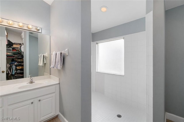 full bath featuring a spacious closet, walk in shower, vanity, and baseboards