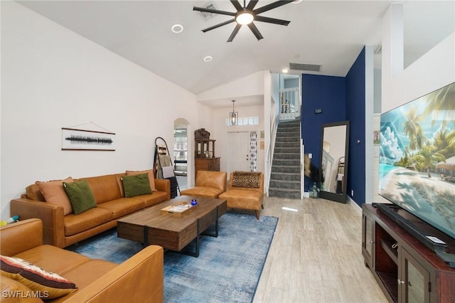 living area with arched walkways, high vaulted ceiling, visible vents, light wood-style floors, and stairs