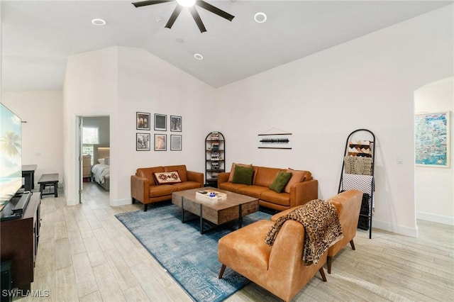 living area featuring arched walkways, vaulted ceiling, light wood-style flooring, and baseboards