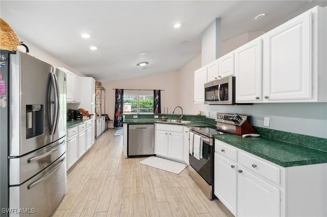 kitchen featuring a peninsula, a sink, white cabinets, appliances with stainless steel finishes, and dark countertops