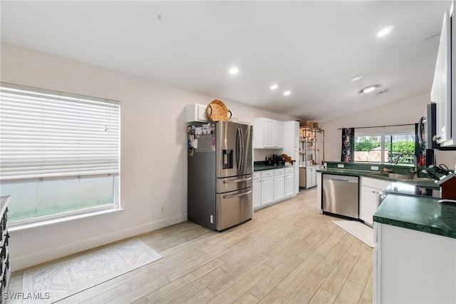 kitchen with white cabinets, dark countertops, light wood-style flooring, stainless steel appliances, and a sink