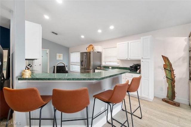 kitchen featuring lofted ceiling, a peninsula, white cabinetry, dark countertops, and stainless steel fridge