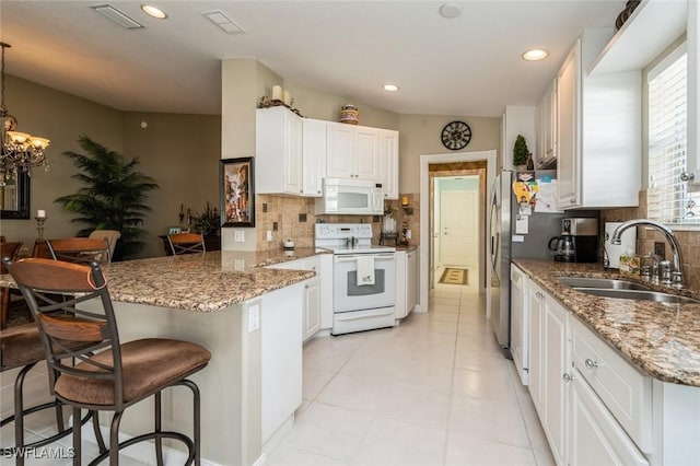 kitchen with a peninsula, white appliances, a sink, white cabinets, and a kitchen bar